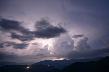 An evening thunderstorm with lightning in the Carpathian mountains, the village of Dzembronya. Dramatic clouds during a thunderstorm pierce the light of lightning in a mountainous area. clipart