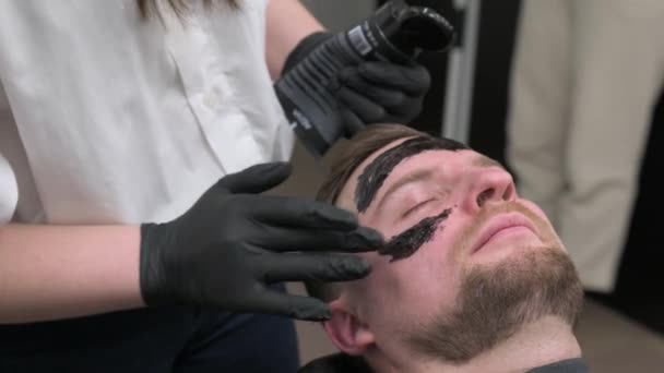 Barber Menerapkan Masker Pelembab Hitam Wajah Seorang Pria Saat Bercukur — Stok Video