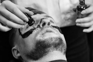 Bir berber stilisti, nemlendirici ve yumuşatmak için müşterilerin sakallarına yağ damlaları sürer. Sakal bakımı.