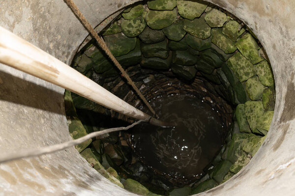 A view of a village well with water, there is a cord and a hose in the well.