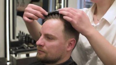 El ile saç şekillendirme, müşterinin saçını bir stilistle tarama. Berber dükkanındaki 4K videosundaki bir ziyaretçinin saç kesimi..