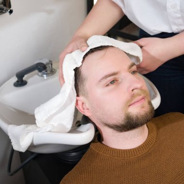 Bir kuaför berber dükkanında yıkandıktan sonra bir müşterinin kafasını beyaz havluyla siler..