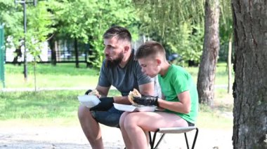 Baba oğul eldiven giyerek sokakta büyük bir hamburger yiyorlar..