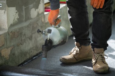 Evin içinde onarım işi, zemini su geçirmez hale getirmek, gaz lambası olan bir adam zifti ısıtıyor..