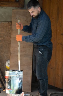 Bir adam ahşap bir sopayla kovada sıvı zifti karıştırır. İnşaat ve tesisat kendi gücüyle ve kendi başına çalışır..