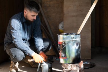 Bir adam ahşap bir sopayla kovada sıvı zifti karıştırır. İnşaat ve tesisat kendi gücüyle ve kendi başına çalışır..