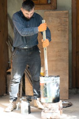 Bir adam ahşap bir sopayla kovada sıvı zifti karıştırır. İnşaat ve tesisat kendi gücüyle ve kendi başına çalışır..