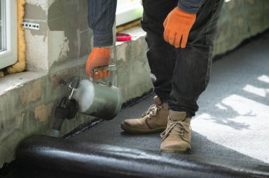 Evin içinde onarım işi, zemini su geçirmez hale getirmek, gaz lambası olan bir adam zifti ısıtıyor..