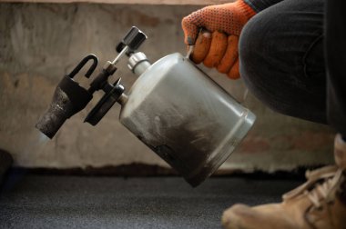 Evin zeminini su geçirmez hale getirmek için bir rulo zifti gaz lambasıyla ısıtan bir adam reçineye yapıştırıyor..