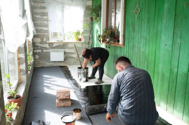 Bir erkek ve bir kadın evin zeminini su geçirmez hale getiriyor, tamirat ve inşaat işleriyle uğraşıyorlar..