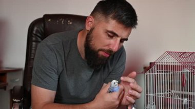 Sakallı bir adam bir papağanı kafesten çıkardı ve elinde tuttu, onunla oynuyordu, küçük mavi bir muhabbet kuşu bir adamın elindeydi..