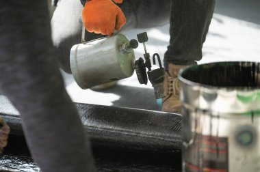 Evin içinde onarım işi, zemini su geçirmez hale getirmek, gaz lambası olan bir adam zifti ısıtıyor..