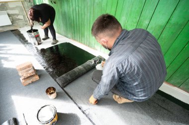 Bir adam zemini su geçirmez hale getirmek için bir rulo zemin ısıtmak için gaz lambası kullanır. Tamir ve inşaat işlerinde çalışır..