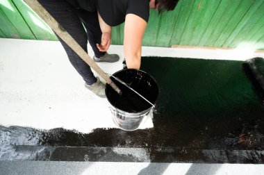 Bir kadın beton zemine zift uygulamak için fırça kullanır. Evin zeminini su geçirmez hale getirir..