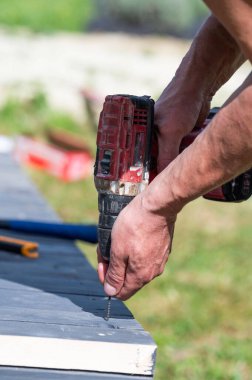 Sanatçı, çardağın tabanını sağlamlaştıran vidaları sıkılaştırmak için bir tornavida kullanıyor..