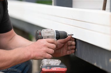 Builder attaches wall to gazebo frame using screws and screwdriver, installation and construction work. clipart