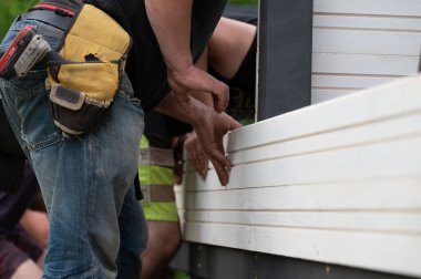 Builder attaches wall to gazebo frame using screws and screwdriver, installation and construction work. clipart