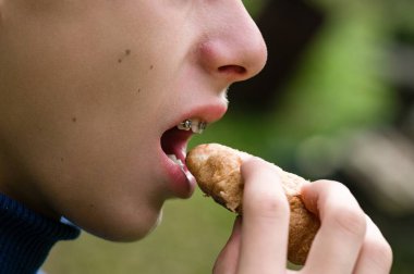 Açık hava hamur işinden hoşlanan genç bir bireyin yakın çekim görüntüsü. Odak noktası yemek yeme eylemi, bulanık yeşil bir arka plan ile.