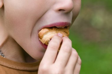 Dolu bir pastadan bir ısırık alan bir çocuğun yakın çekimi. Odak noktası ağız ve el ele tutulması, bulanık yeşil bir arka plan ile.