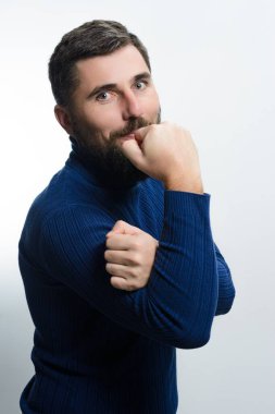 Mavi balıkçı yaka kazaklı sakallı bir adam, eli çenesinde, açık bir arkaplanda dalgın dalgın bakıyor. Düşünceli ifadesi tefekküre ya da karar verme mekanizmasına işaret ediyor..