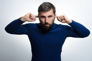 Mavi kazak giyen, sakallı bir adam, kulaklarını parmaklarıyla kapatıyor, bir hayal kırıklığı ya da gürültüyü engelleme arzusu taşıyor..