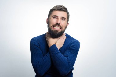 Acı dolu bir suratı olan sakallı bir adam iki eliyle boğazını hafifçe kavrıyor. Boğuluyor ya da rahatsızlanıyor gibi görünüyor..