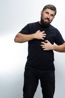 Siyah gömlek ve kot pantolon giyen sakallı bir adam iki eliyle göğsünü kaşıdı. Rahatsız görünüyor, deri tahrişi ya da alerji olduğunu gösteriyor..