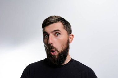 Sakallı, ağzı açık beyaz bir arkaplan karşısında şaşkınlık içinde şaşırmış bir adamın vesikalığı. İfadesi şok ve güvensizlik içeriyor..