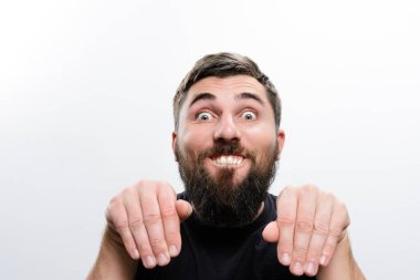 Beyaz bir arka plana karşı sakallı bir adam şakacı, aptal bir yüz ve el hareketleriyle mizah ve hafiflik sergiliyor..
