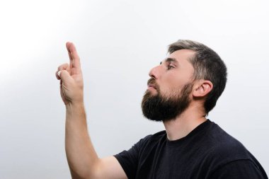 Sakallı bir adamın beyaz bir arka planda parmaklarını çaprazlarken yan görüntüsü. Umut dolu bir ifadeyle yukarı bakıyor..