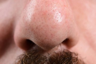 Bir adamın burnunun detaylı makro görüntüsü, deri dokusu ve gözenekleri. Burun deliklerinin altında koyu bıyık kılları görünür..