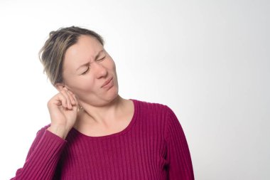 Gözleri kapalı, kulağına dokunan, rahatsızlık ya da acı taşıyan bir kadın. Sade bir arka planda kestane rengi bir kazak giyiyor. Bu da potansiyel kulak ağrısı ya da diğer işitsel sorunları akla getiriyor..