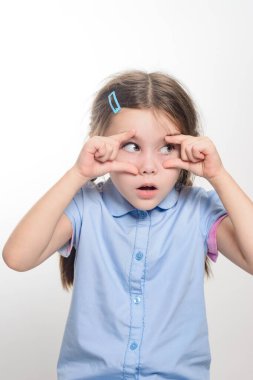 Parmaklarının arasından neşeyle bakan bir kızın portresi. Açık mavi bir gömlek giyiyor ve yüzünde tuhaf bir ifade var. Arkaplan düz beyaz.