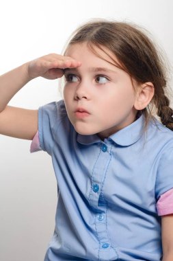 Kahverengi saçlı, açık mavi tişörtlü, meraklı bir genç kız gözlerini güneşten koruyor..