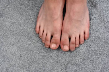 Yüksek açılı, yakın plan bir çift çıplak ayakla pofuduk gri bir havluya nazikçe yerleştirilmiş. Görüntü bir sakinlik ve rahatlama hissi veriyor..