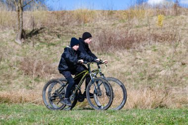 Parlak ve güneşli bir günde dağ bisikleti süren iki genç çocuk bir yol boyunca bisiklet sürüyor. Sıcak ceketler ve şapkalar giyip, dışarıda eğleniyorlar..