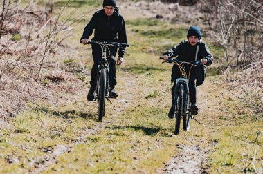 İki genç çocuk kirli bir yolda bisiklet sürüyor, güneş ışığı yolculuklarını aydınlatıyor. Sahne kırsal ve doğal, tasasız bir keşif hissi uyandırıyor..