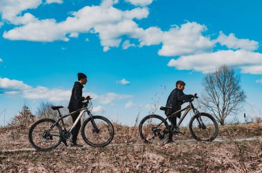 Parlak, güneşli bir gün. Toprak yolda yürüyen iki genç, her biri bisiklet itiyor. Gökyüzü, tüylü beyaz bulutları olan canlı bir mavidir. Barışçıl bir açık hava sahnesi.