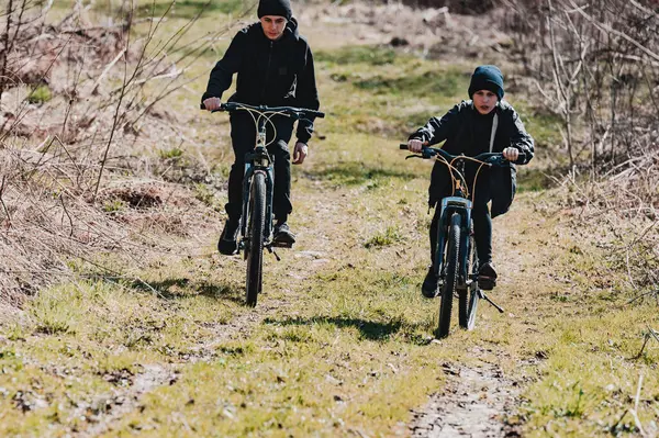 İki genç çocuk kirli bir yolda bisiklet sürüyor, güneş ışığı yolculuklarını aydınlatıyor. Sahne kırsal ve doğal, tasasız bir keşif hissi uyandırıyor..