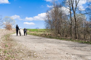 İki genç çocuğun çakıllı bir patika boyunca bisikletlerini yürüttüğü sakin bir sahne. Parlak mavi gökyüzünün altındaki kırsal alan sakin ve huzurlu bir gün olduğunu gösteriyor..