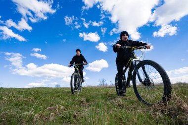 İki genç, yemyeşil bir arazide bisiklet sürerek güneşli bir günün tadını çıkarırlar. Uçsuz bucaksız mavi gökyüzü ve kabarık bulutlar güzel bir zemin yaratır..