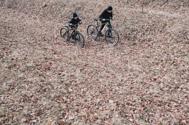 İki genç sonbahar yapraklarıyla kaplı bir patika boyunca dağ bisikletlerine biniyor. Sakin bir açık hava sahnesi, eğlence ve doğa görüntüsü için mükemmel..
