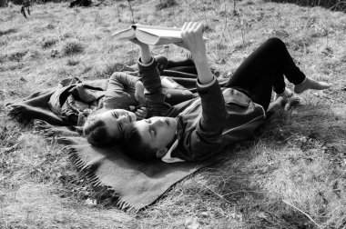 İki küçük kardeş, çimenli bir tarlada bir battaniyeye uzanmış, bir kitabı paylaşıyorlar. Sahne huzurlu ve bir rahatlama ve kardeş bağı hissi uyandırıyor..