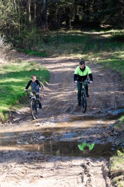 Bir adam ve bir çocuk güneşli bir dağ bisikletinin keyfini çıkarıyorlar. Ormanlık alanda çamurlu bir patikada geziniyorlar. Eğlenceli bir aile aktivitesi sergiliyorlar..