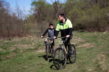 Baba ve oğul tarlada bisiklet sürüyor. Doğada aileyle aktif eğlence..
