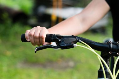 A person's hand firmly holds the handlebars of a bicycle. The background is blurred, showing a green field. The image suggests outdoor activity and leisure.