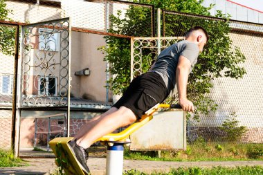 Genç bir adam açık hava spor aletleri üzerinde bir kuvvet alıştırması yapıyor. Odaklanmış ve kararlı, temiz havada egzersiz yapıyor..