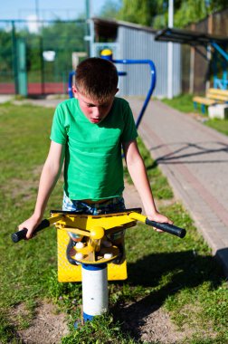 Odaklanmış genç bir çocuk sarı bir spor aleti kullanır. Yeşil bir gömlek giyiyor ve güneşli ortamda sağlıklı ve aktif bir yaşam tarzı var..