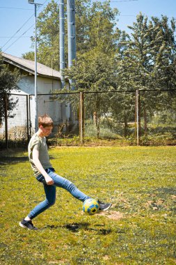 Genç bir insan güneşli bir günün tadını çıkarıyor, çimenli bir alanda ustalıkla futbol topunu tekmeliyor. Sahne huzurlu ve sıradan bir açık hava eğlencesi..