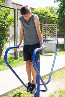 Genç bir adam parktaki mavi paralel barlara daldırıyor. Gri bir gömlek ve koyu bir şort giyiyor. Sahne güneşli ve açık..